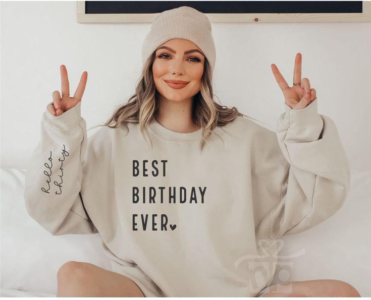 a woman sitting on top of a bed with her hands in the air and two peace signs