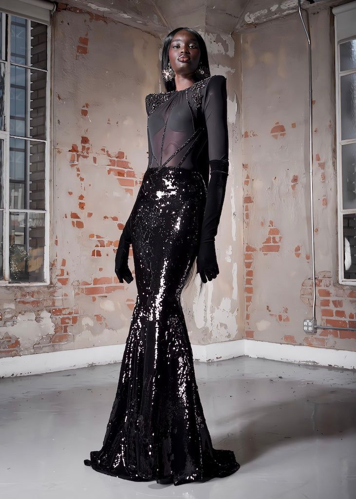 a woman in a black and silver dress standing next to a brick wall with an open window