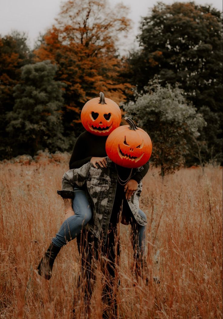 two people hugging each other in a field with pumpkins on their heads and faces