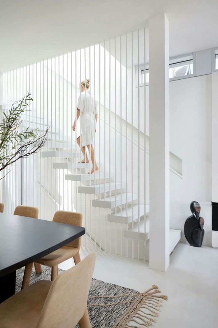 a man walking up the stairs in a white room next to a table and chairs