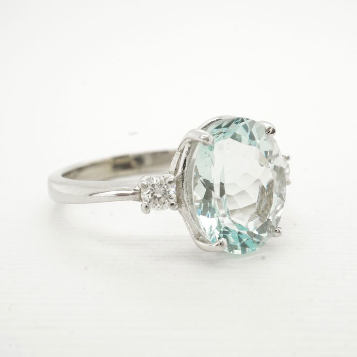 A classic oval blue Aquamarine with 2 round brilliant diamonds in solid 14 karat white gold. This gorgeous ring with cool watery colors that will leave you feeling refreshed! This oval baby blue Aquamarine is accompanied by two white Diamonds accent the Aqua for extra sparkle. Made with recycled 14k gold and would be an exceptional engagement ring or something special for a March birthstone ring. Genuine Aquamarine 2.59 carat Oval, faceted Genuine AquamarineFaint Greenish / Baby Blue Very Slight Oval Aquamarine Diamond Ring In White Gold, Oval Aquamarine Diamond Ring With Prong Setting, 14k White Gold Oval Topaz Ring, Oval Aquamarine Diamond Ring Fine Jewelry, Oval Aquamarine Diamond Ring In Fine Jewelry Style, Oval Aquamarine Diamond Ring With Diamond Accents, Oval Aquamarine Diamond Ring With Accents, Oval Aquamarine Ring In White Gold, Oval Aquamarine Ring With Diamond Accents