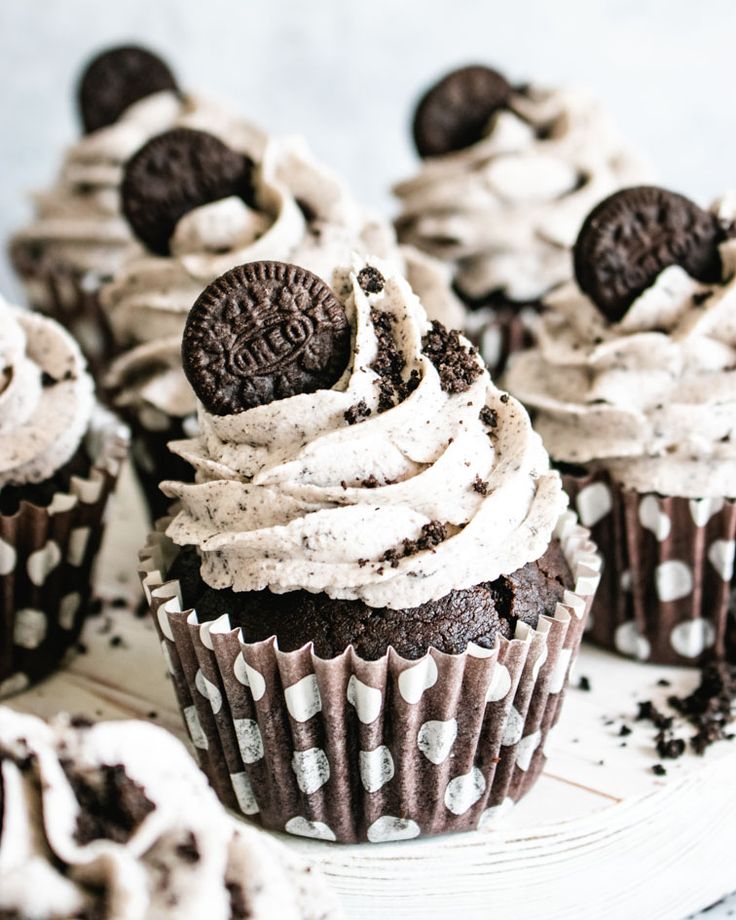 chocolate cupcakes with white frosting and oreo cookies on top sitting on a plate