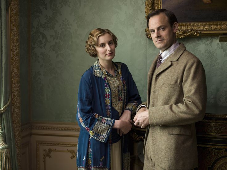 a man and woman standing next to each other in front of a painting on the wall