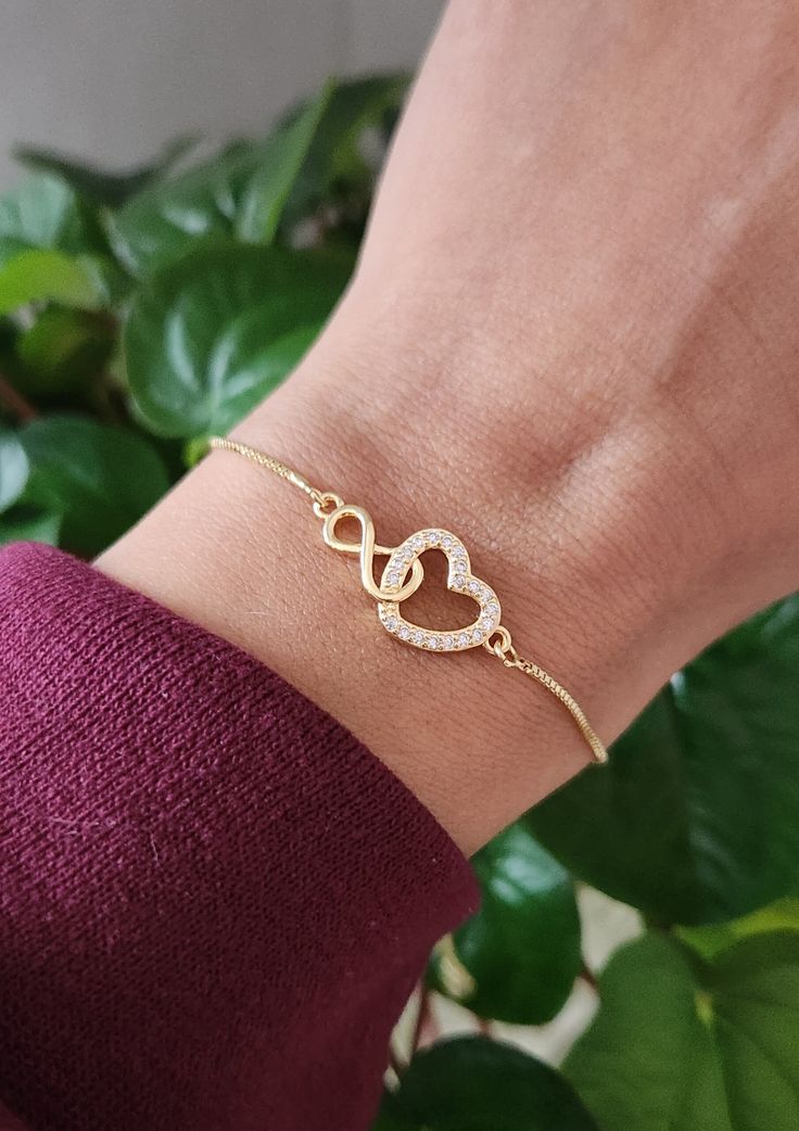 "This 18K gold bracelet is made with gold a linked heart & infinity on a gold adjustable chain. Heart & infinity measures approximately 1\" x .5\" (heart).  The gold brass chain has a ball and joint closure that slides to adjust to the size you need. It can fit almost any size wrist. Slide the ball to the end in order to slide the bracelet over your hand onto your wrist. Slide the ball to tighten it to the size you desire. The remaining chain dangles with 2 small crystals at the ends. This fits most wrist sizes (5-9\")." Adjustable Gold Bracelet For Valentine's Day, Gold Plated Infinity Jewelry As A Gift, Gold Plated Infinity Jewelry Gift, Gold-plated Infinity Jewelry Gift, Elegant Hypoallergenic Chain Bracelet For Valentine's Day, Valentine's Day Adjustable Chain Bracelet, Adjustable Dainty Gold Bracelet For Valentine's Day, Adjustable Chain Bracelet For Anniversary, Gold Double Heart Jewelry With Adjustable Chain