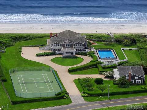 an aerial view of a large house with a tennis court in the front yard and ocean in the background