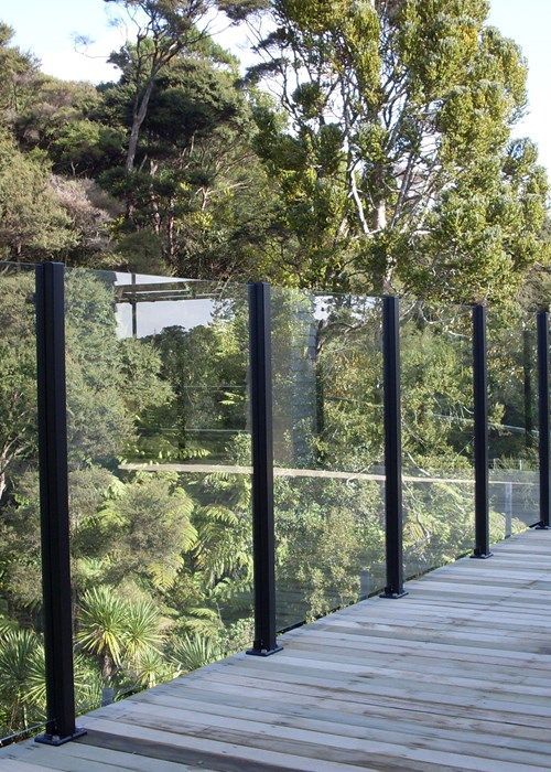 a wooden deck with black railings and trees in the backgroung area