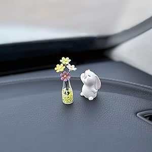 two small figurines sitting on the dashboard of a car with flowers in it