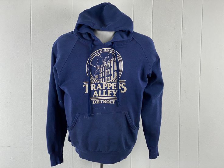 "Vintage 1970s, maybe ealy 80s hooded sweatshirt Hoodie. Made of blue poly/cotton. Detroit Michigan sweatshirt. TRAPPERS ALLEY was an area of Greektown in Downtown Detroit. I used to play pinball down there as a child. Now it has been reconstructed into a huge Casino. Has a front pocket and drawstring hood. No name label, size large. Actual measurements are:  48\" around the chest  42\" around the waist   22\" shoulder to shoulder  23\" shoulder  to cuff    25\" overall length, plus 12\" hood In good condition, slightly distressed with some paint and some spots." Blue Vintage Hoodie With Drawstring Hood, Vintage Cotton Hoodie, Vintage Cotton Hooded Hoodie, Vintage Cotton Hooded Sweatshirt, Vintage Hoodie With Drawstring For Fall, Vintage Cotton Hoodie With Double-lined Hood, Vintage Long Sleeve Hoodie With Drawstring, Vintage Cotton Hoodie For Fall, Vintage Sweatshirt With Double-lined Hood For Streetwear