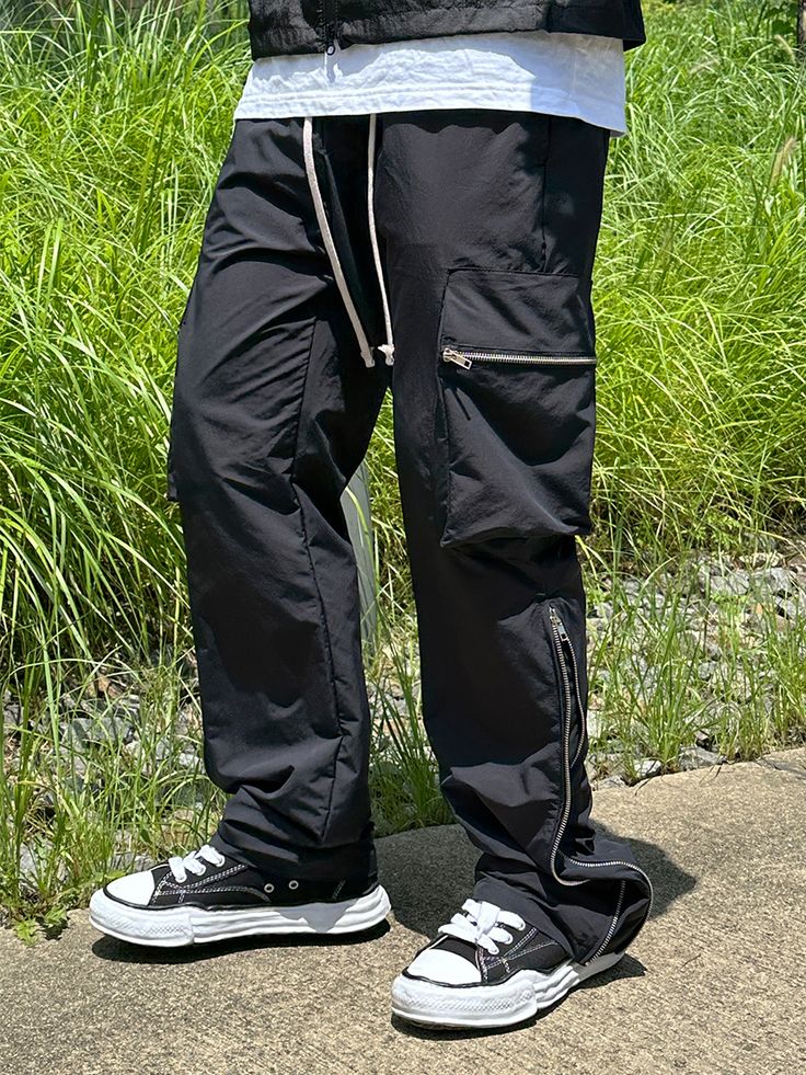 Editor's NoteCLACO's Nylon Side Zipper Cargo Pants are made out of nylon 100% fabric that has a subtle glow and light weight. With the side zippers extending up to up to the knees that makes the fit wider, you can style it in various ways. It has adjustable string on the waistband for comfortable wear. You can style it with various items for casual, relaxed, and trendy look during various seasons. - Adjustable waistband with string- Side zippers- Side cargo pockets- Adjustable silhouetteMeasurements (in.)M/L- Waist: 14.17 in / 14.96 in- Thigh: 12.60 in / 13.39 in- Rise: 12.60 in / 12.99 in- Hem: 8.27 in / 8.66 in- Length: 40.94 in / 41.73 inModel info: Height 5'11, Weight 169 lbs, Wearing size LComposition & Care- Nylon 100%- Refer to care labelDesigner- by CLACO Techwear Cargo Pants With Zipper For Streetwear, Nylon Cargo Pants With Zip Fly For Outdoor, Nylon Pants With Zip Fly For Outdoor, Outdoor Nylon Cargo Pants With Zip Fly, Nylon Outdoor Pants With Zip Fly, Utility Parachute Pants With Zip Fly For Outdoor, Urban Black Cargo Pants With Zipper Closure, Black Urban Cargo Pants With Zipper Closure, Black Nylon Techwear Bottoms