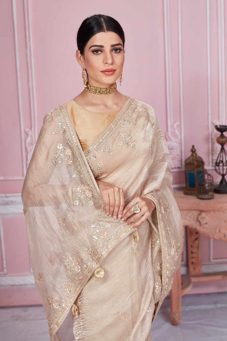 Flaunt your elegant style on festive occasions in this stunning beige embroidered tissue silk saree. It comes with a matching blouse piece. Disclaimer: The shown stitched blouse on the model is for display purpose only. The saree comes with a matching blouse piece and finished with fall and piko. Cream Saree With Intricate Embroidery For Festivals, Festive Beige Blouse Piece With Traditional Drape, Beige Semi-stitched Saree, Gold Blouse Piece With Intricate Embroidery In Tissue Silk, Gold Tissue Silk Blouse Piece With Intricate Embroidery, Designer Raw Silk Cream Saree, Cream Saree With Intricate Embroidery For Diwali, Designer Cream Raw Silk Saree, Diwali Cream Saree With Intricate Embroidery