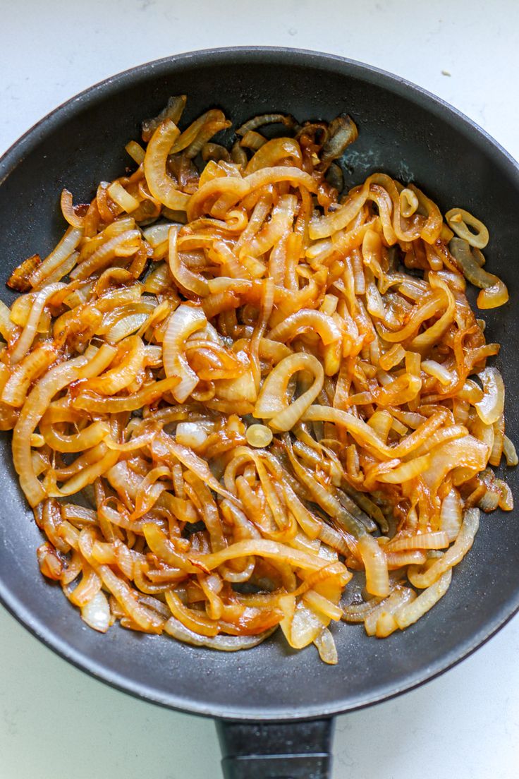 a skillet filled with noodles and onions on top of a white counter next to a knife