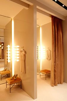 a dressing room with lights on the wall and clothes hanging in front of it's mirrors