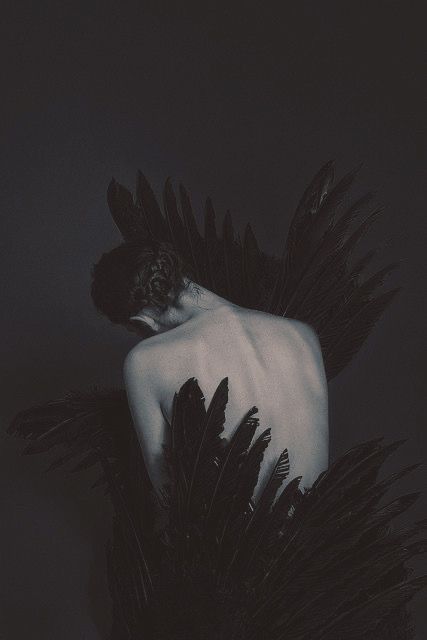 a black and white photo of a naked man with feathers on his back, in the dark