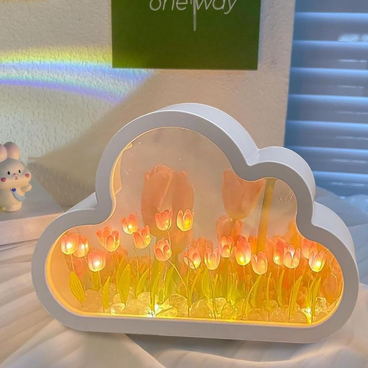 there is a cloud shaped light up display on the table with flowers in front of it