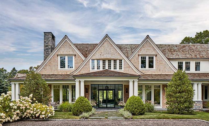 a large house with white trim and shingles on the roof, surrounded by greenery