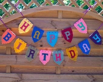 a birthday banner with the words happy on it is hanging from a wooden fence in front of a trellis