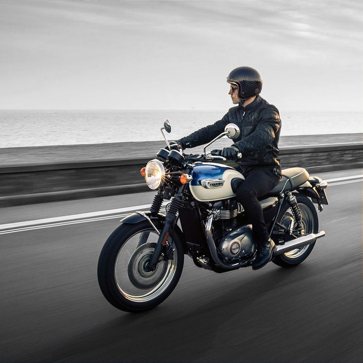 a man riding on the back of a motorcycle down a road next to the ocean