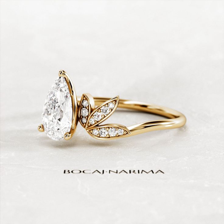 a gold ring with a pear shaped diamond in the center and leaves on each side