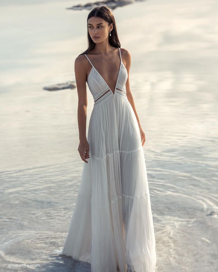 a woman is standing in the water wearing a white dress with straps and an open back