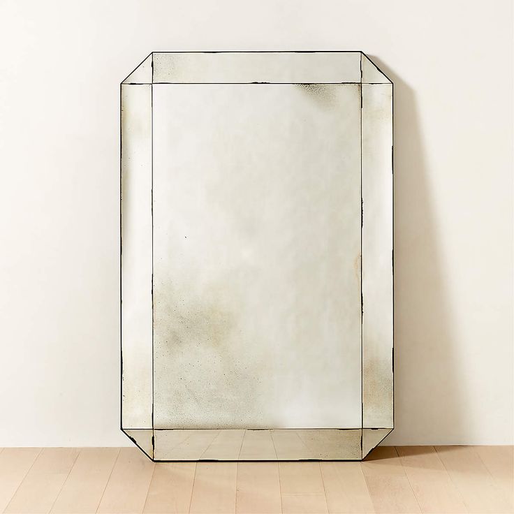 a mirror sitting on top of a wooden floor next to a white wall with a black frame