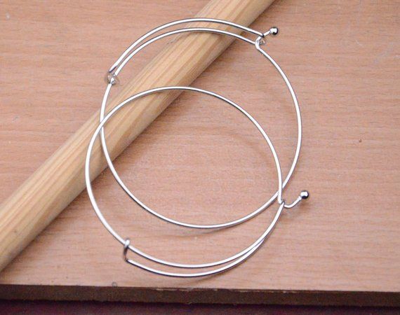 two silver hoop earrings sitting on top of a wooden table next to a pencil and piece of wood