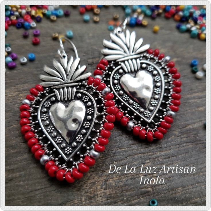 "Inola Earrings Materials:  Sterling Silver plated hooks, Silver plated Pewter heart, Czech Glass Beads, 10k Gold plated hooks, Gold plated Pewter heart  Length:  2.5\" Inspired by Mexican Folk Art & the colorful embroidery crafted throughout Latin America.  I wrapped czech glass beads in red & silver around these gorgeous milagro sacred hearts.  Choose from Silver or Gold. The sacred heart is a symbol of everlasting love & commitment. Your earrings will be very similar to the ones shown, but du Traditional Red Heart-shaped Jewelry, Nickel Free Heart Shaped Jewelry For Festivals, Traditional Heart-shaped Jewelry With Heart Beads, Nickel-free Heart-shaped Jewelry For Festival, Bohemian Heart-shaped Earrings With Dangling Beads, Bohemian Heart Bead Dangle Earrings, Bohemian Dangle Heart Earrings With Heart Beads, Bohemian Heart Beaded Dangle Earrings, Nickel Free Heart Earrings For Festivals