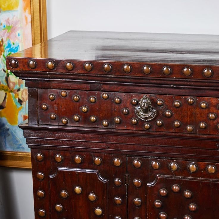 an old wooden chest with brass rivets on the top and bottom drawers, in front of a painting