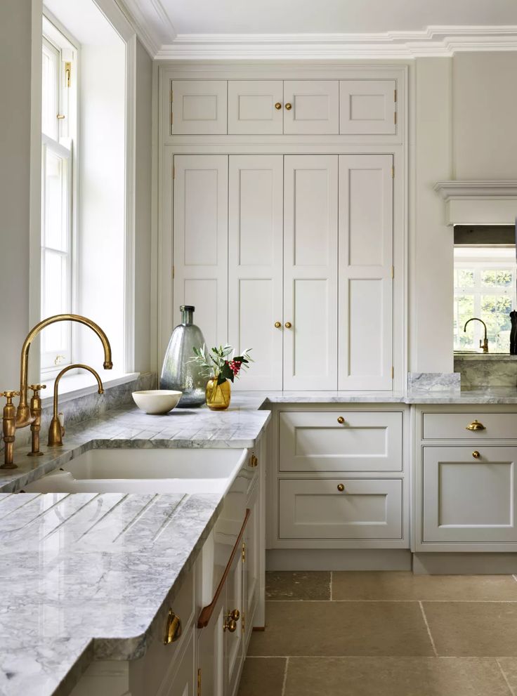 a kitchen with white cabinets and marble counter tops, gold faucets and vases