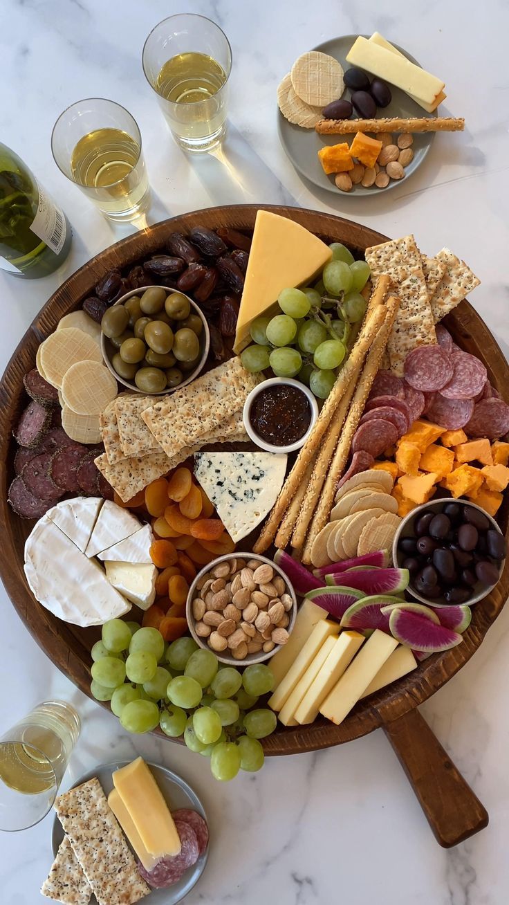 a wooden platter filled with cheese, crackers and grapes