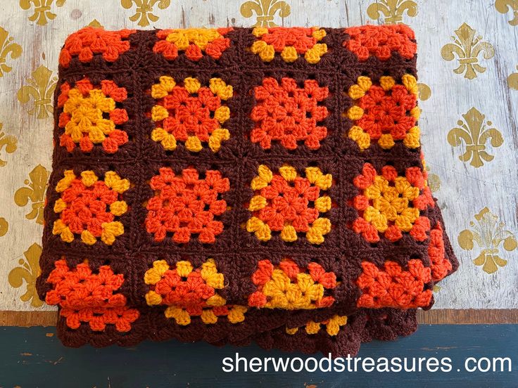 an orange and brown crocheted blanket sitting on top of a wooden table next to a wall