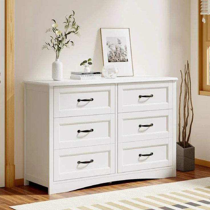 a white dresser with drawers and pictures on top