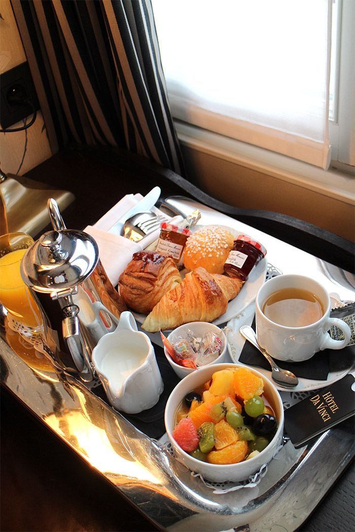 a breakfast tray with coffee, croissants and fruit on it in front of a window