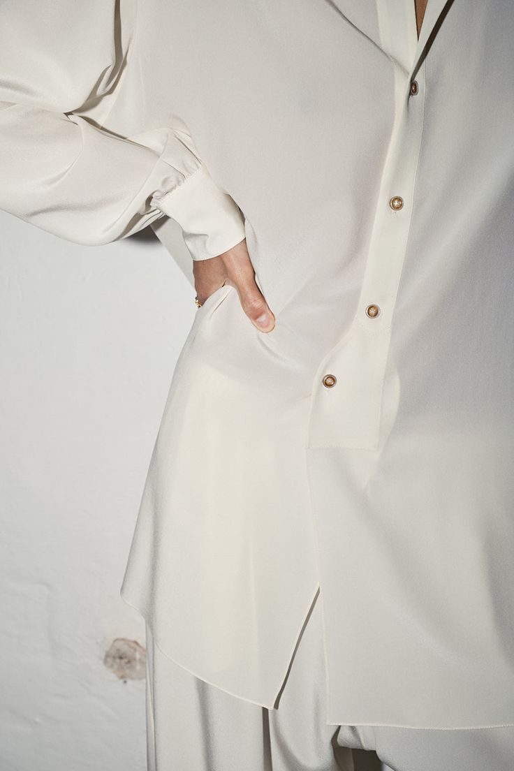 Oversized and relaxed fit. Shirt Collar Curved front and back hem. Back of the shirt fits longer than the front. Exposed Buttons. Mother pearl buttons. French seam finish Fits comfortably across shoulders, falls loose throughout the body. Oversized full-length sleeves with pleats and mother pearl button cuffs. Full-length sleeves with pleats and button cuffs Colour: Nata (Cream) One Size fits S/M/L Model is 1´82 - 5’10" Unisex 100% Pure Silk. Crepe de ChineMADE IN SPAIN Elegant Oversized Blouse With Shirttail Hem, White Long Sleeve Blouse With Hidden Button Closure, Elegant Shirt Dress With Shirttail Hem For Work, Oversized Formal Button-up Blouse, Elegant Shirt Dress With Shirttail Hem And Relaxed Fit, Elegant Shirt Dress With Relaxed Fit And Shirttail Hem, Elegant Shirt Dress With Button Cuffs And Shirttail Hem, Timeless Long Sleeve Blouse With Button Cuffs, Elegant Shirttail Hem Shirt Dress With Relaxed Fit