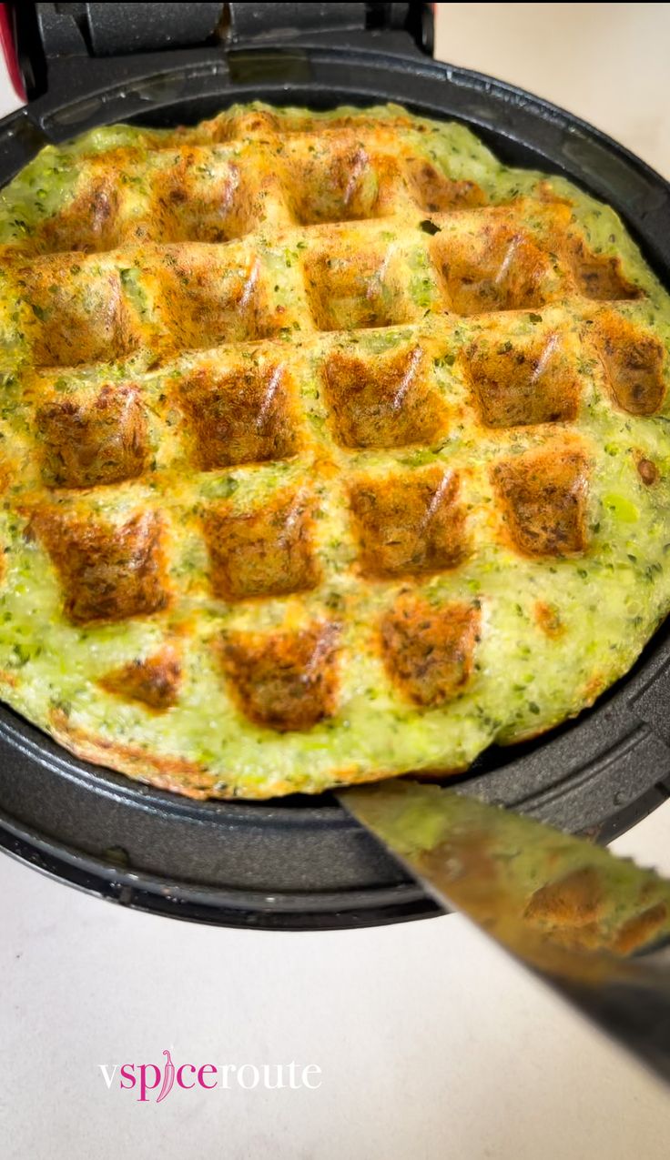 a waffle topped with meatballs and cheese on a black plate next to a knife