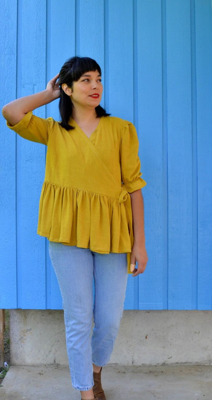 a woman standing in front of a blue wall with her hand on her head and wearing jeans