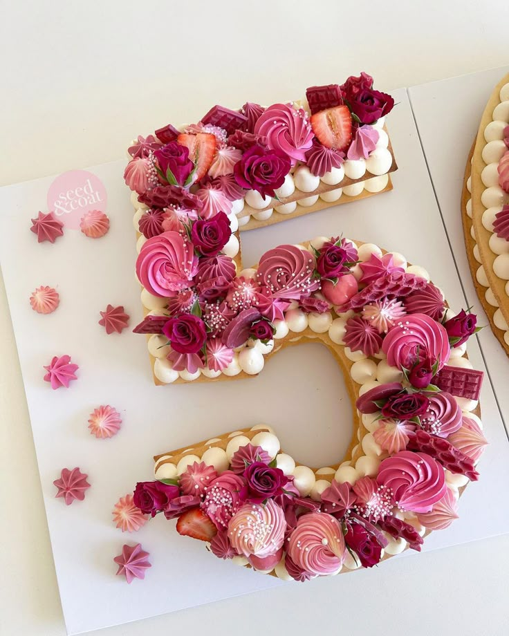 the number five is decorated with flowers and icing on a sheet of paper next to two cakes