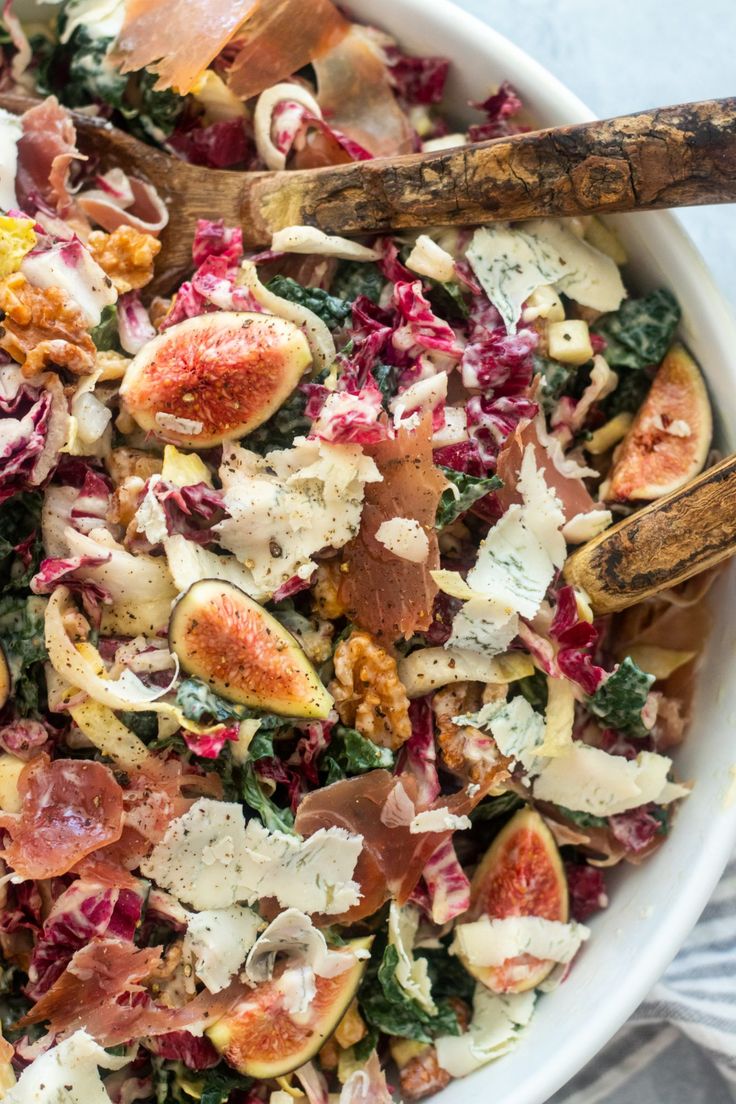 a white bowl filled with lots of different types of food and two wooden spoons