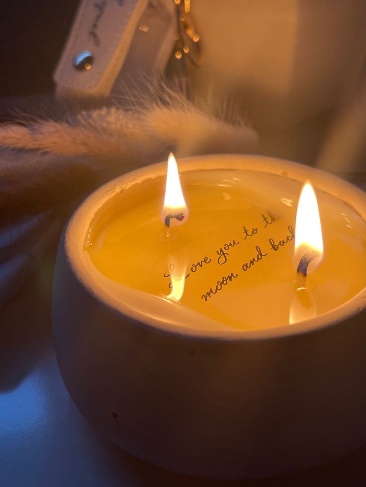 three lit candles in a white bowl with writing on it and some feathers next to them