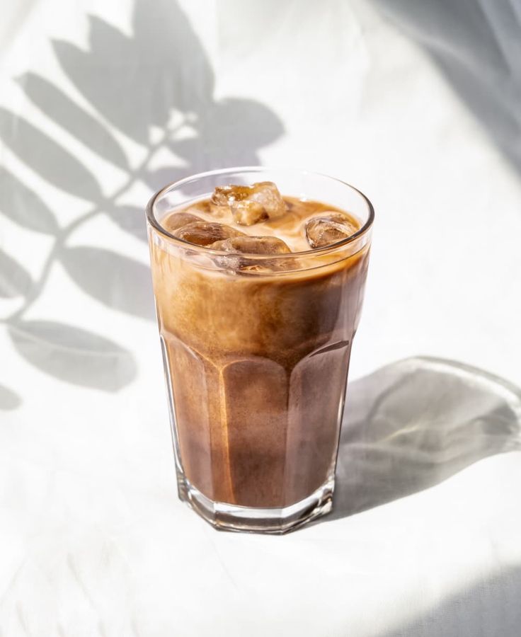 an iced drink is sitting on a white surface with the shadow of a plant behind it