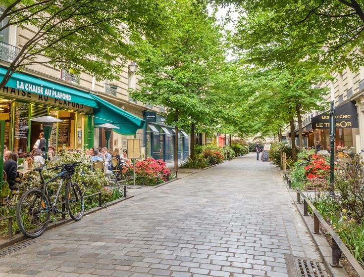 a cobblestone street lined with shops and people sitting at tables in front of them