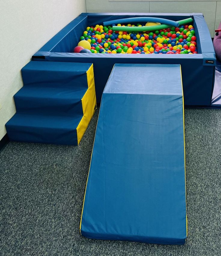 an indoor play area for children with blue walls and colorful balls in the pool, on carpeted flooring