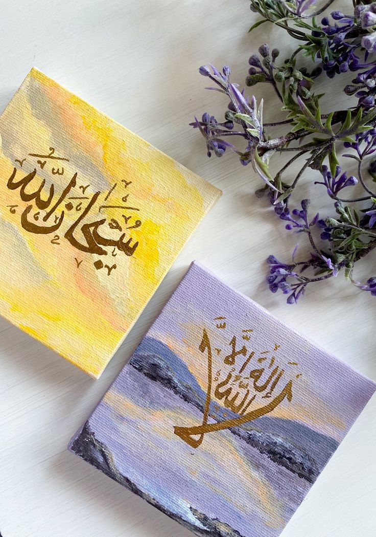 two paintings with arabic writing on them sitting next to some purple and yellow flowers in the background