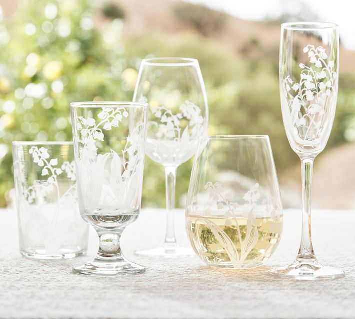 four wine glasses with white flowers on them sitting on a table next to each other