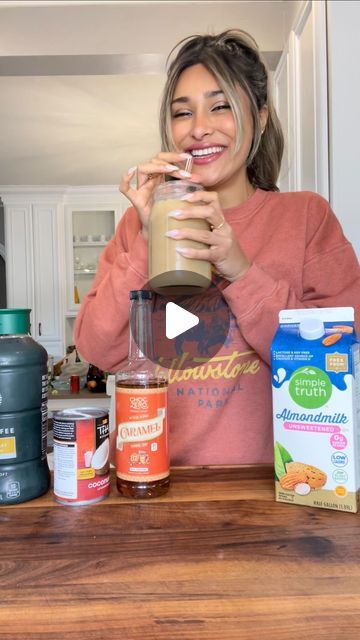 a woman standing in front of a counter holding a blender with ingredients on it