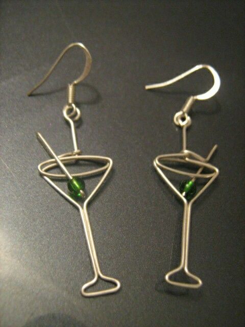 a pair of wine glasses with green beads are shown on a black surface and one is made out of silver wire