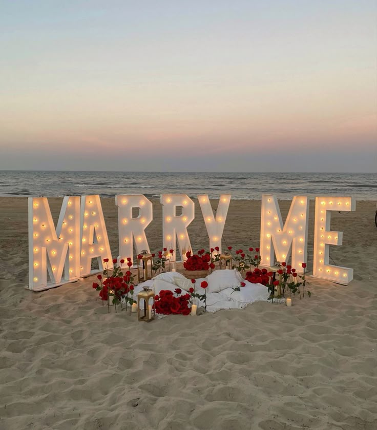 a sign that says marry me on the beach with flowers and candles in front of it