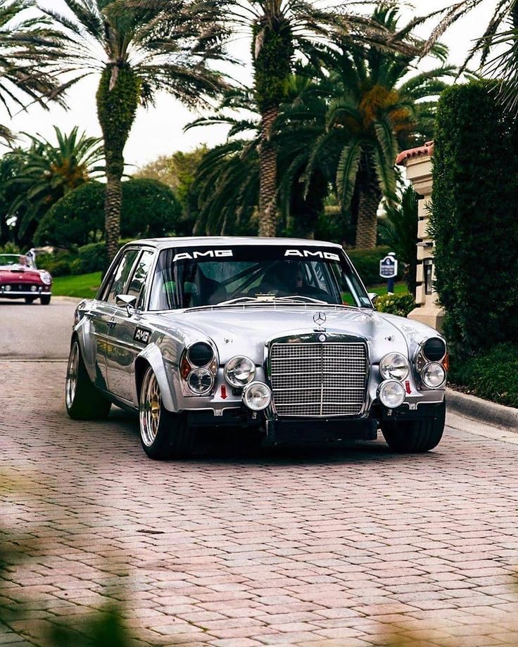 an old car is parked on the side of the road near some palm trees and bushes