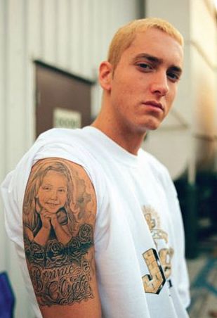 a man with a tattoo on his arm standing in front of a door and looking at the camera