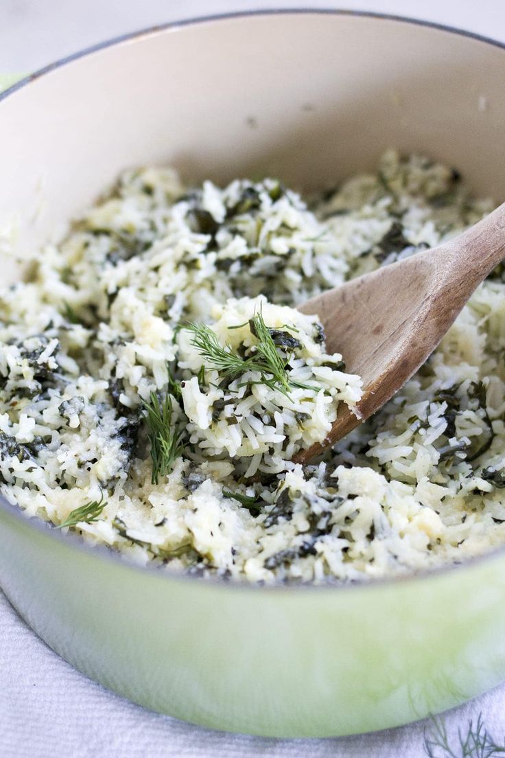 a wooden spoon in a pot filled with white rice and spinach sprinkled with herbs