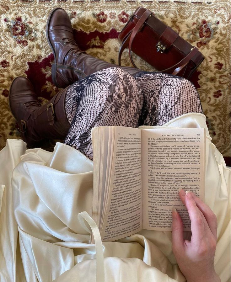 a woman laying on top of a bed with an open book next to her legs